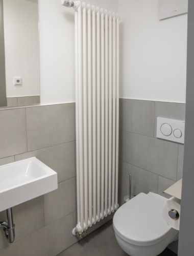 Heller Toilettenraum mit grauen Fließen bis zur halben Höhe