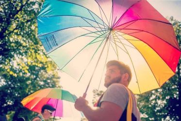 Diakon Marcel Renner der einen Regenbogen-Regenschirm trägt, durch den helles Sonnenlicht fällt